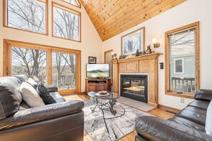 A spacious living room with a fireplace, large windows, and a television.
