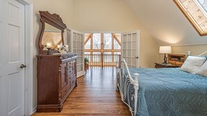 A bedroom with a sloped ceiling, a large window, a bed, a dresser, and a nightstand. - Dreamers Inn by Taylor Made Deep Creek (Swanton)