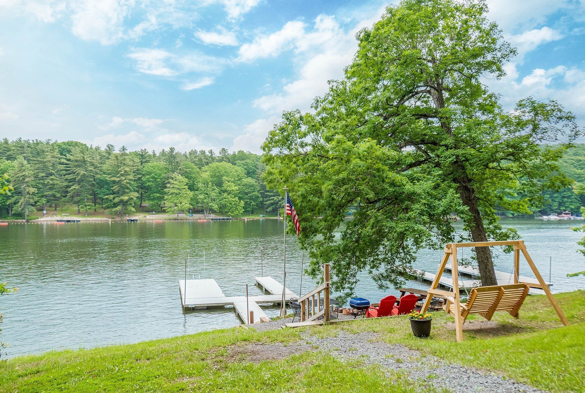 A lakeside deck with a swing, dock, and outdoor seating.