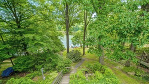 A lush garden with a wooden deck leading to a lake, surrounded by dense foliage and a small bridge. - Dreamers Inn by Taylor Made Deep Creek (Swanton)