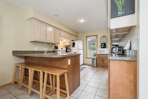 Cocina moderna con armarios de madera, una isla central con taburetes, refrigerador, microondas y cafetera.