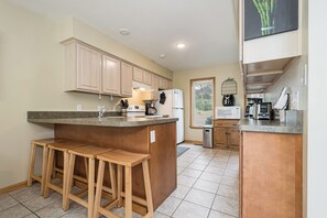 A modern kitchen with wooden cabinets, a central island with stools, a refrigerator, a microwave, and a coffee maker.
