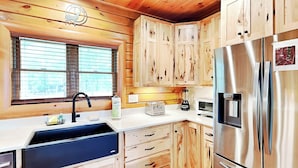 A modern kitchen with wooden cabinets, stainless steel appliances, a sink, and a window with blinds. - Eagle on 7 by Taylor Made Deep Creek (McHenry)
