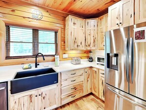 A modern kitchen with wooden cabinets, stainless steel appliances, a sink, and a window with blinds. - Eagle on 7 by Taylor Made Deep Creek (McHenry)