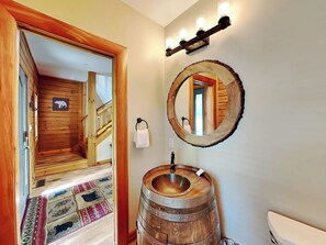 A wooden interior with a wooden barrel sink, a mirror, and a wooden staircase.