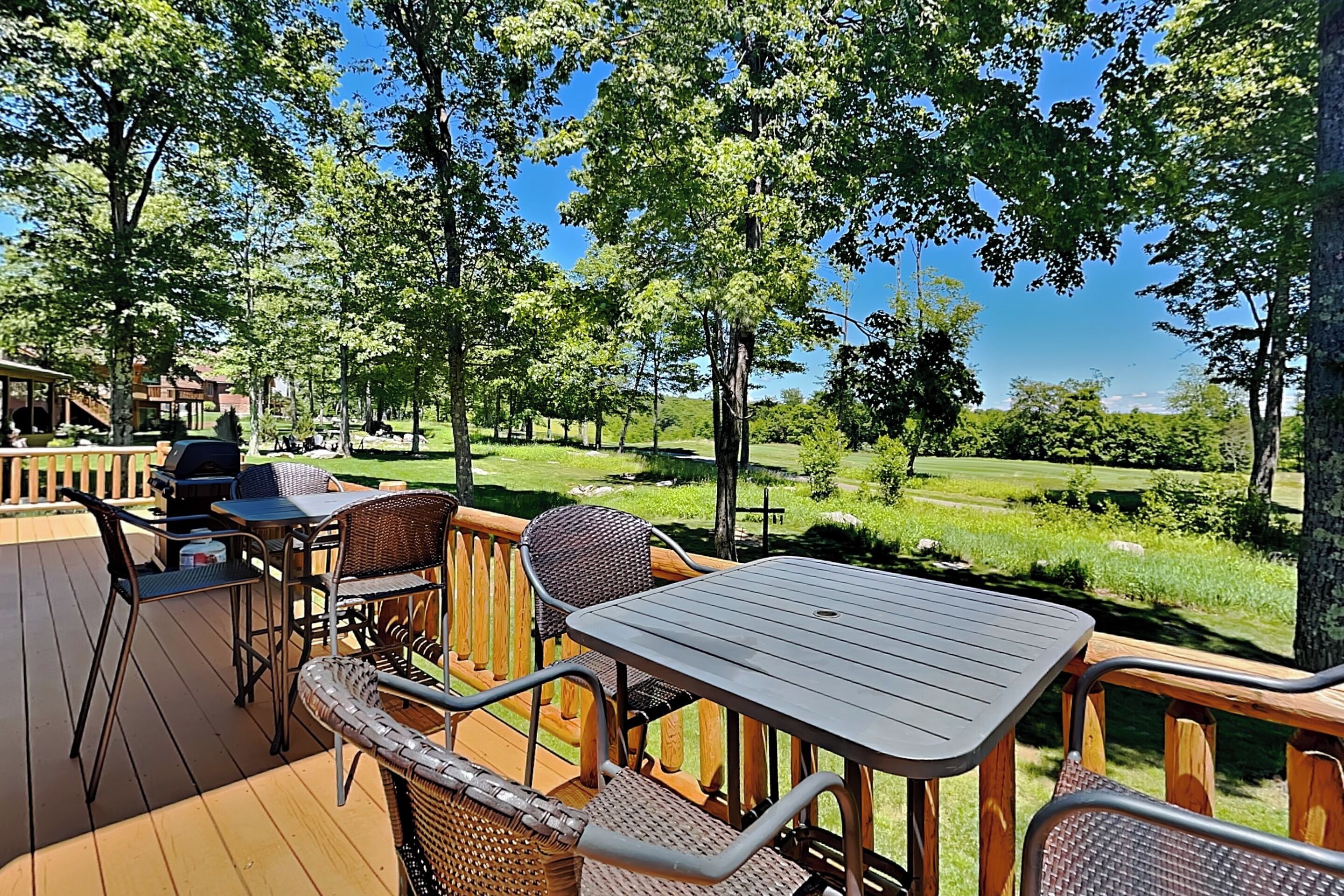 An outdoor deck with a table and chairs, overlooking a grassy area and trees.