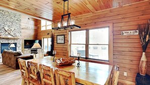 A rustic wooden interior with a dining area, stone fireplace, and large windows. - Eagle on 7 by Taylor Made Deep Creek (McHenry)