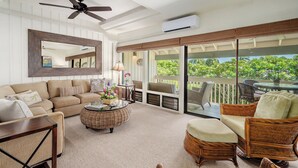 Ein geräumiger Wohnbereich mit einer Couch, Sesseln, einem Couchtisch und einem Balkon mit Gartenmöbeln.
