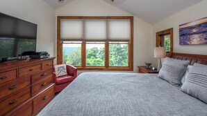 Ein Schlafzimmer mit einem großen Bett, einem Fernseher auf einer Holzkommode, einem Fenster mit Jalousien, einem Deckenventilator und einem Bild an der Wand.