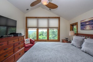 A bedroom with a large bed, a TV on a wooden dresser, a window with blinds, a ceiling fan, and a painting on the wall. - Eagle's Rest by Taylor Made Deep Creek (McHenry)