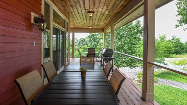 Eine überdachte Veranda mit einem Holztisch und Stühlen, einem Grill und Blick auf eine grüne Landschaft.