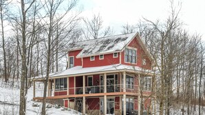 Ein großes, zweistöckiges Haus mit roter Fassade und einem Balkon, umgeben von Bäumen und Schnee.