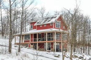 A large, two-story house with a red exterior and a balcony, surrounded by trees and snow. - Eagle's Rest by Taylor Made Deep Creek (McHenry)