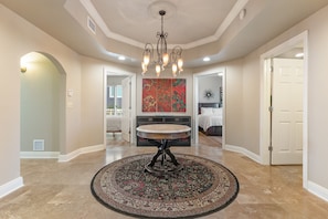 A spacious hallway with a round table in the center, a chandelier, and a large abstract painting on the wall.