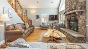 A spacious living room with a stone fireplace, a wooden staircase, and a comfortable seating area.