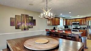 A modern kitchen with wooden cabinets, a central island with a round wooden table, and a unique antler chandelier.