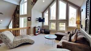 A spacious living room with a high ceiling, large windows, a fireplace, and a cozy seating area.