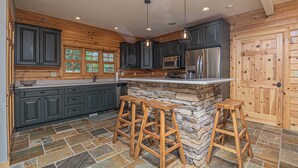 A kitchen with dark cabinets, a stone island, and wooden stools. - Family Sanity by Taylor Made Deep Creek (McHenry)