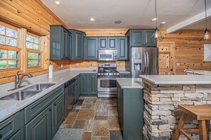 A modern kitchen with green cabinets, a stone accent wall, and a central island. - Family Sanity by Taylor Made Deep Creek (McHenry)