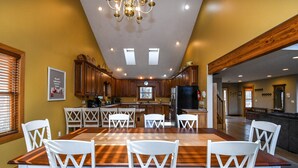 Un'ampia cucina con mobili in legno, un grande tavolo da pranzo con sedie bianche e un lampadario.
