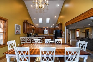 A spacious kitchen with wooden cabinets, a large dining table with white chairs, and a chandelier.