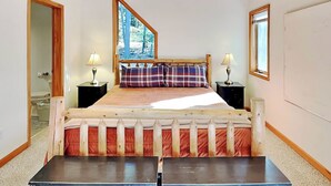 A bedroom with a wooden ceiling, a large window, a bed with plaid bedding, two bedside tables with lamps, and a small table in front of the bed. - Fir Reel by Taylor Made Deep Creek (Oakland)