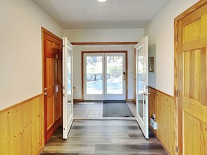 A hallway with wooden doors and a view of a landscaped area outside.