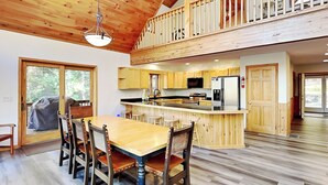 A spacious kitchen with wooden cabinets, a central island, and a dining area with a large table and chairs. - Fir Reel by Taylor Made Deep Creek (Oakland)