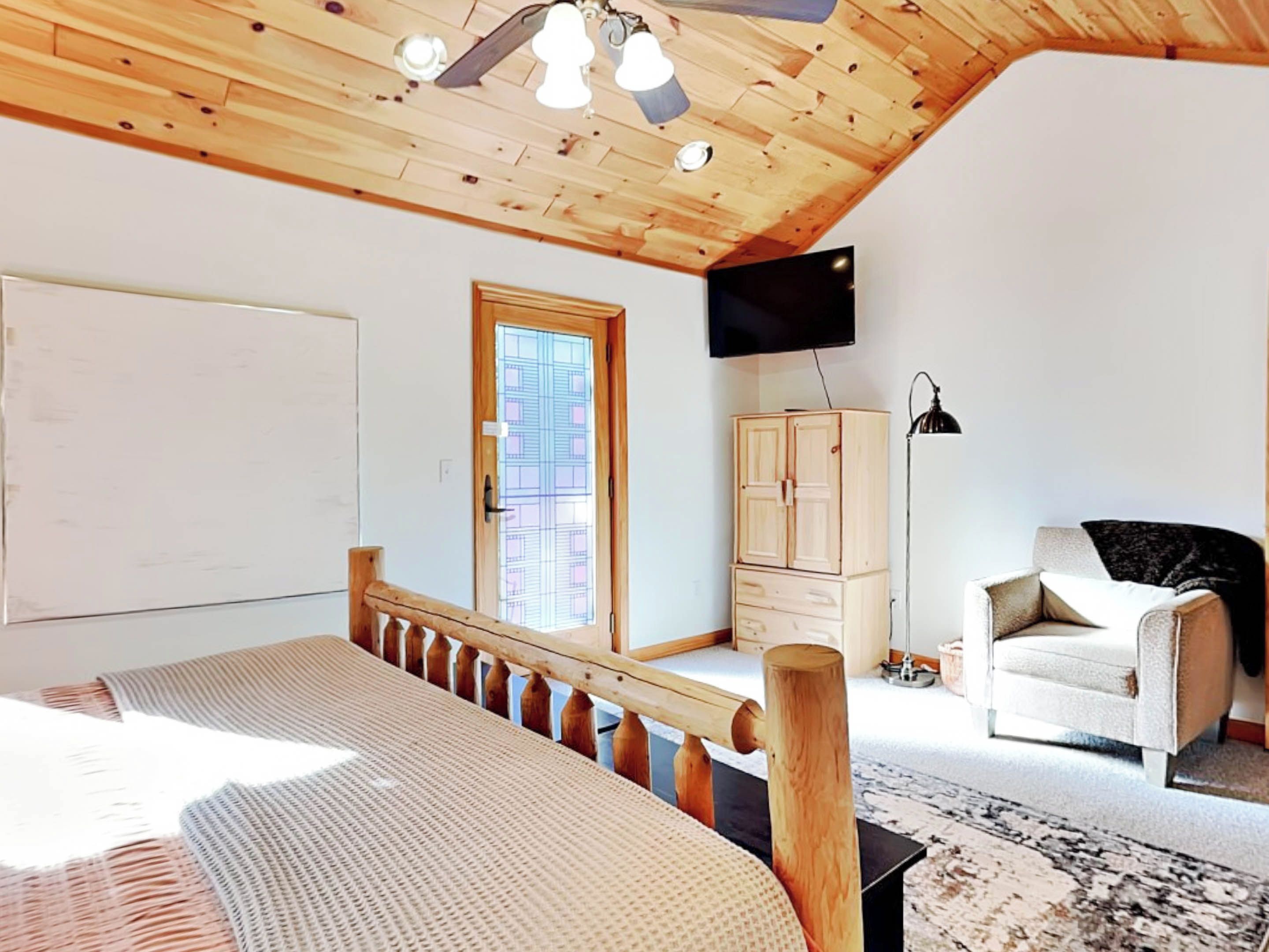 Une chambre avec un plafond en bois, un lit, une télévision, une armoire et une chaise.