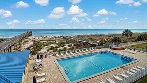 Zona de piscina con vistas a la playa y al océano, rodeada de tumbonas y sombrillas.