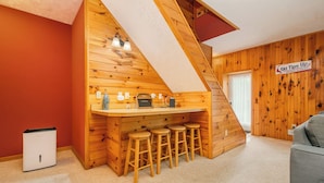 Interior acogedor de una cabaña con una barra de madera, una escalera y un letrero que dice 'Tips Up'.