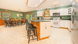 Una cocina con una isla central, armarios blancos, un refrigerador de acero inoxidable y una zona de comedor con sillas de madera.
