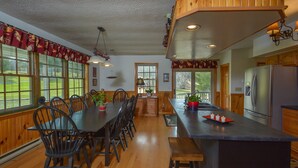 Une cuisine spacieuse avec des meubles en bois, un grand îlot central doté de tabourets et un coin repas avec une longue table et des chaises.