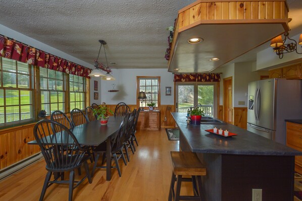 A spacious kitchen with wooden cabinets, a large island with stools, and a dining area with a long table and chairs.