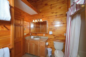 A wooden cabin bathroom with a sink, mirror, and toilet.