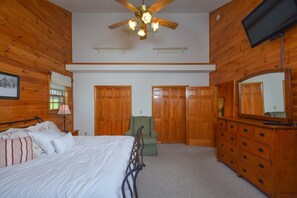 A bedroom with a bed, wooden wardrobe, a green armchair, a ceiling fan, and a TV mounted on the wall. - Forever Young by Taylor Made Deep Creek (McHenry)