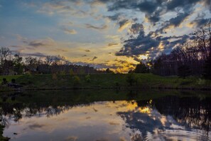 A calm lake reflecting the sky with clouds, surrounded by trees and a grassy area. - Forever Young by Taylor Made Deep Creek (McHenry)