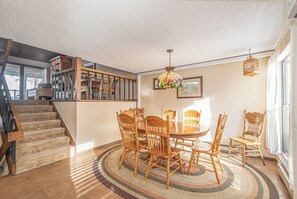 Un espace repas avec une table et des chaises en bois, un tapis à motifs et un escalier menant à une mezzanine.