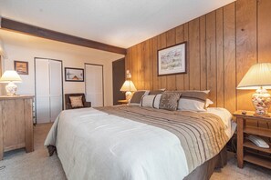 Un dormitorio con una cama grande, paneles de madera, una mesita de noche con lámpara y un aparador.