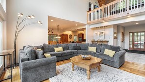 A spacious living area with a grey sectional sofa, a wooden coffee table, and a large window. - Friday's Escape by Taylor Made Deep Creek (McHenry)