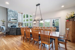 A spacious dining area with a large wooden table and chairs, a stone fireplace, and large windows offering views of the outdoors. - Friday's Escape by Taylor Made Deep Creek (McHenry)