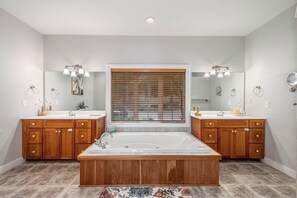 A bathroom with two sinks, a large bathtub, wooden cabinets, and a window with blinds. - Friday's Escape by Taylor Made Deep Creek (McHenry)