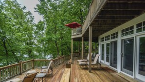 A wooden deck with outdoor furniture, a red umbrella, and a view of trees. - Friday's Escape by Taylor Made Deep Creek (McHenry)
