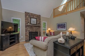 A living room with a stone fireplace, a television on a cabinet, a sofa with striped pillows, and a lamp on a table.