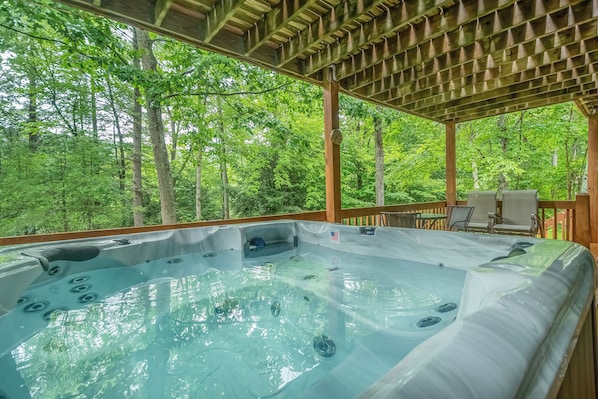 A hot tub area with a wooden deck and a view of a forest.