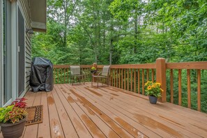 A wooden deck with a railing, two chairs, a covered grill, and potted plants. - Georgia's Place by Taylor Made Deep Creek (Swanton)