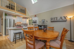 A spacious kitchen with white cabinets, a central island, and a dining area with wooden chairs and a table.
