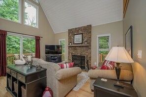 A cozy living room with a stone fireplace, a flat-screen TV, and comfortable seating. - Georgia's Place by Taylor Made Deep Creek (Swanton)