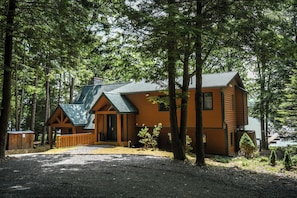 A cabin with a green roof, wooden exterior, and a gravel driveway.
