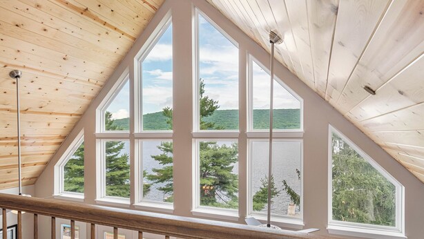 A room with a sloped ceiling and large windows offering a view of a lake and forest. - Glencoe by Taylor Made Deep Creek (Oakland)
